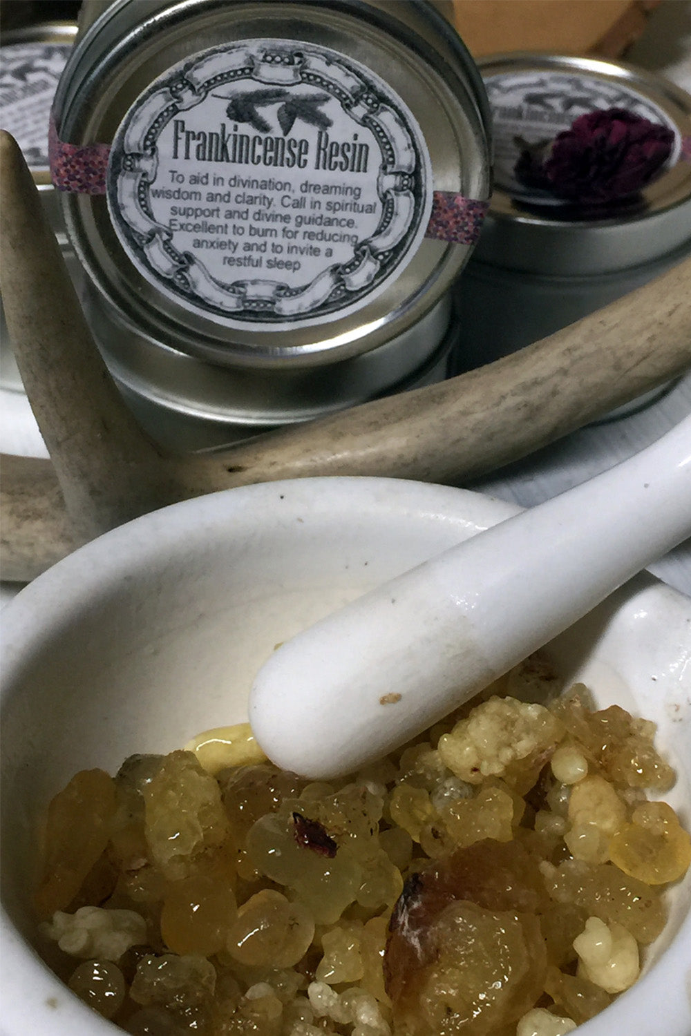  A mortar and pestle sit on a rustic wooden surface, with natural resin being ground into fine powder. A few drops of oil are added to the mixture, ready to infuse into a luxurious perfume. The rich texture of the resin and the smooth motion of the pestle create an artisanal, hands-on approach to crafting a unique fragrance. The scene evokes a sense of timeless tradition and care, blending nature’s raw ingredients into something truly special