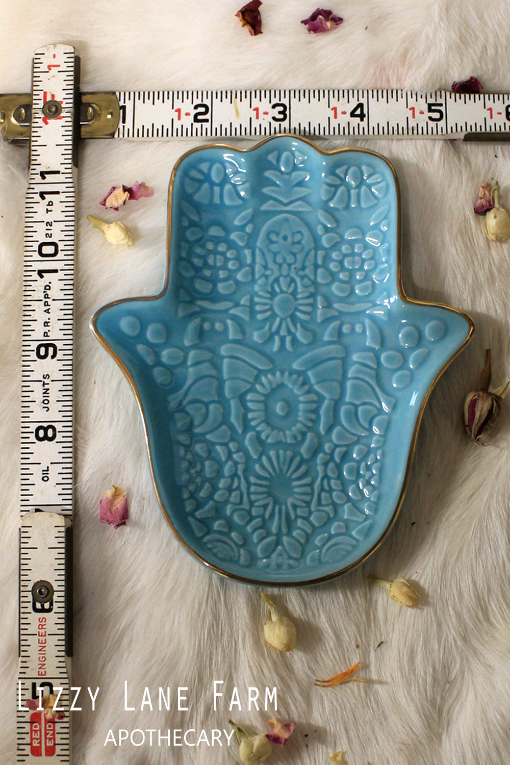 A vibrant teal Hamsa hand smudge plate takes center stage in this beautifully arranged smudge kit. Intricate details and a gold-tone rim enhance the spiritual design, while surrounding it are the thoughtfully curated supplies: a mini white sage smudge stick, a braided sweet grass bundle, a palo santo stick, hand-rolled Styrax incense, a hand-carved soapstone heart, a Chinese Qing Dynasty coin charm, and rain-scented incense matches. All these items are neatly packaged in a rustic burlap pouch, ready to brin