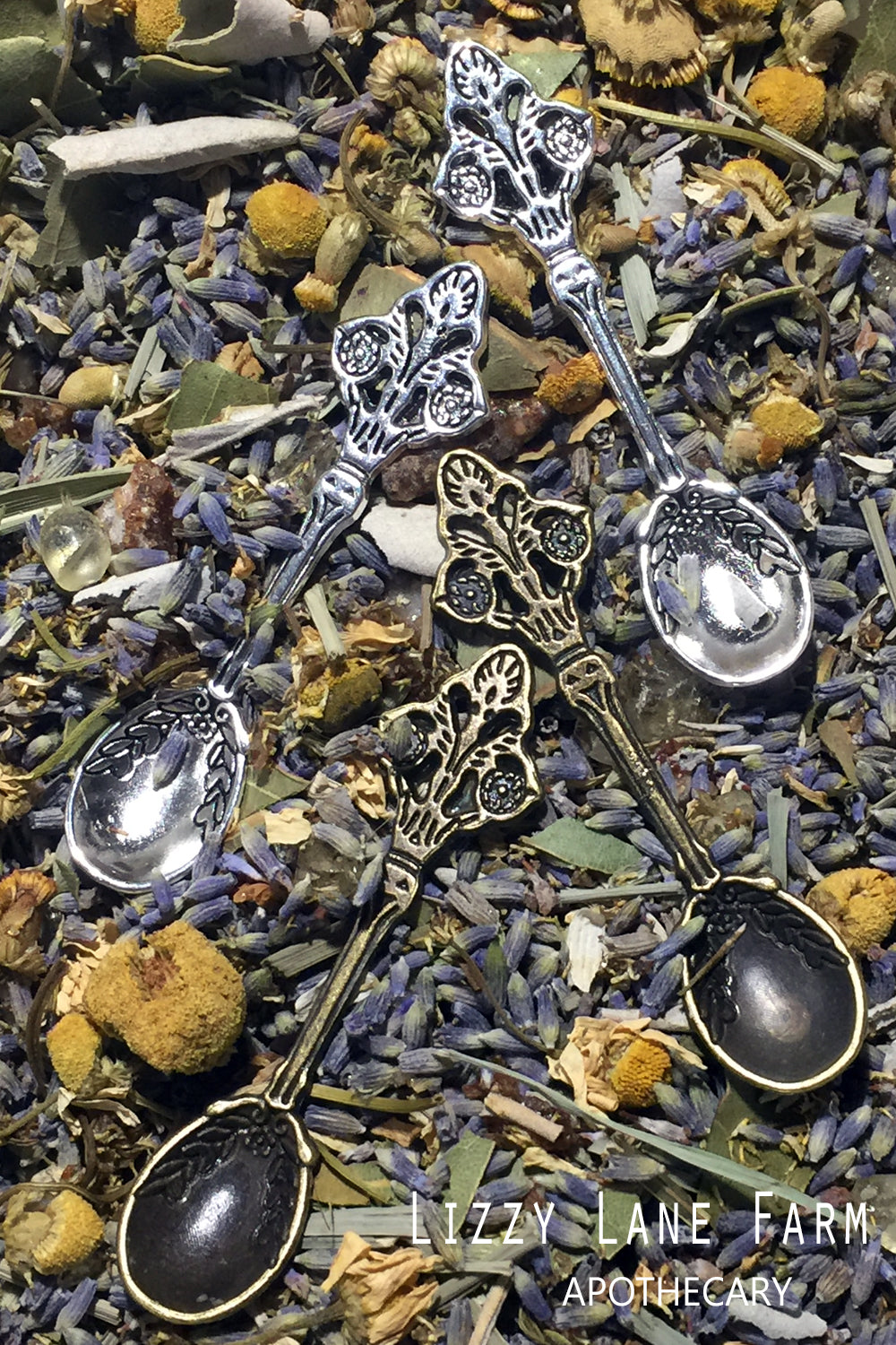 A close-up of two metal herbal spoons, one in silver tone and one in brass, elegantly resting on a bed of herbs. These petite spoons are part of our incense accessory kit, ideal for measuring and sprinkling loose incense or herbal blends.