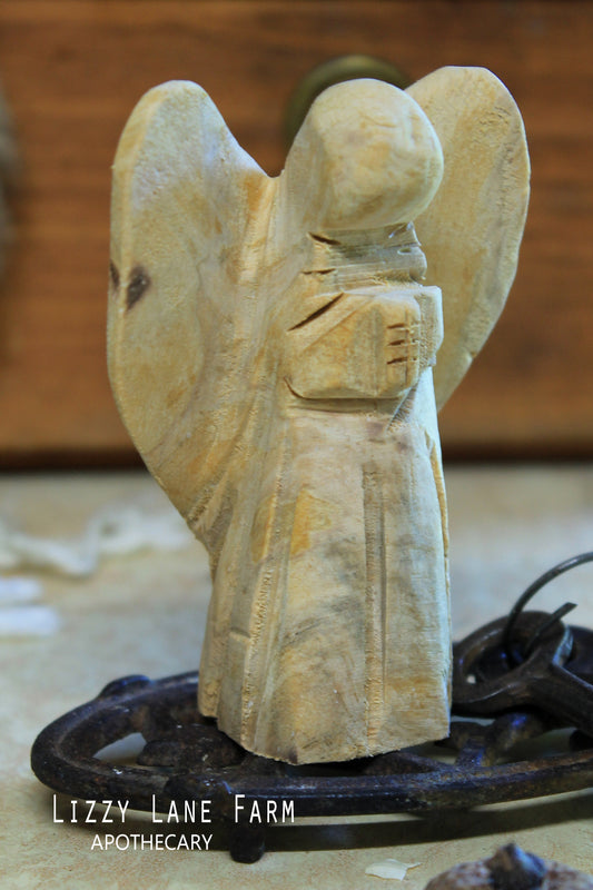 A smooth hand-carved wooden angel made from palo santo, standing upright on soft linen. Visible grain, warm tone, and gentle carved curves under natural light.
