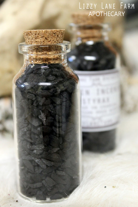 A small glass cork-top bottle filled with Black Styrax Resin,  The rich, dark resin is visible through the clear glass, offering a glimpse of its texture and deep color. The bottle’s classic design adds a touch of elegance to any home or ritual space, perfect for daily relaxation practices and slow living